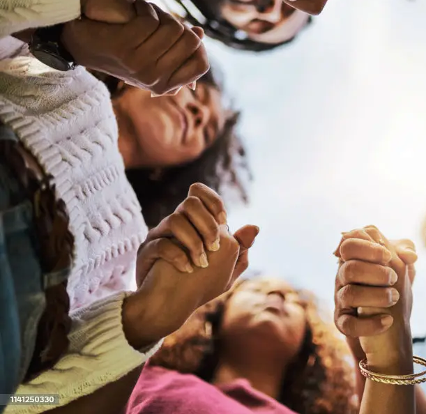 Black women holding hands praying together. Join our private facebook group